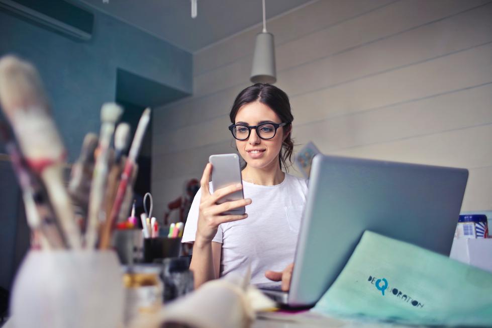 Woman looking at her phone in front of a laptop